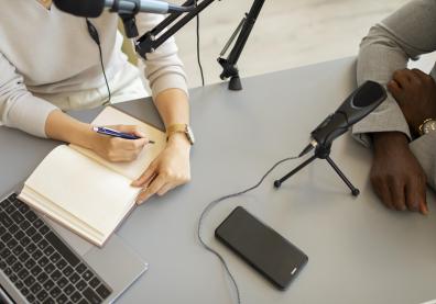 Mains de deux femmes sur une table devant des micros, écrivant sur un cahier