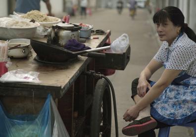 Une cuisinière de rue est assise sur un tabouret devant sa table dans les rues de Shanghai