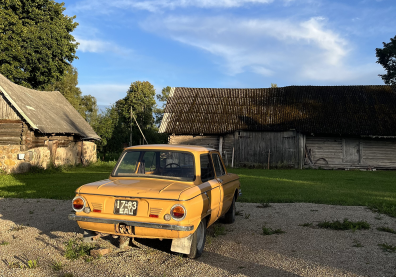 Photo d'une vieille voiture jaune avec en face et sur le côté gauche des vieilles bâtisses