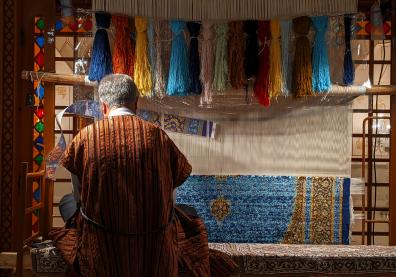 Un homme assis de dos tisse un tapis