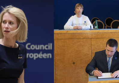 A gauche, jeune femme blonde avec un haut bleu et une broche avec le drapeau estonien, à droite : une femme assise sur un pupitre qui regarde de haut un homme en costume qui signe un papier