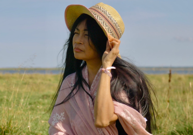 Portrait d'une femme dans un champ, elle porte sa main à son chapeau 