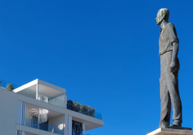 Une statue d'un homme qui regarde le haut d'un immeuble avec un ciel bleu