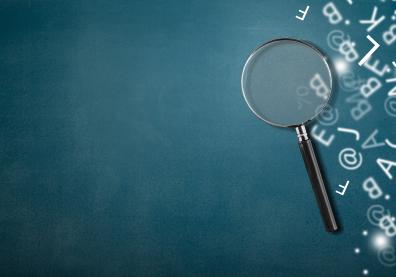 A magnifying glass with part of scattered english alphabet letters on the desk background