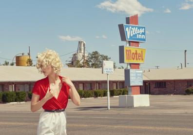 Photo of a blonde woman with curly hair in a motel parking lot