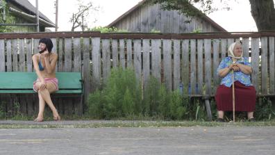Deux femmes sont assises sur deux bancs a l'extrémité du cadre de la photo, devant une clôture. A gauche une jeune femme en maillot de bain et à droite une vieille dame avec une canne