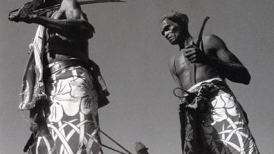 Deux hommes torse nus tiennent des bâtons et marchent en ronde 