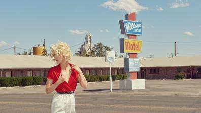Photo of a blonde woman with curly hair in a motel parking lot