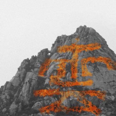 Photographie en noir et blanc d'une montagne sur laquelle est peint en orange un idéogramme chinois