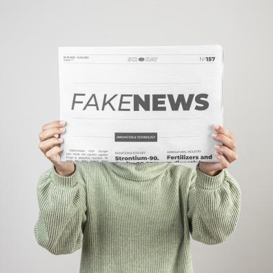 Quelqu'un tient un journal devant son visage avec l'inscription "fake news"