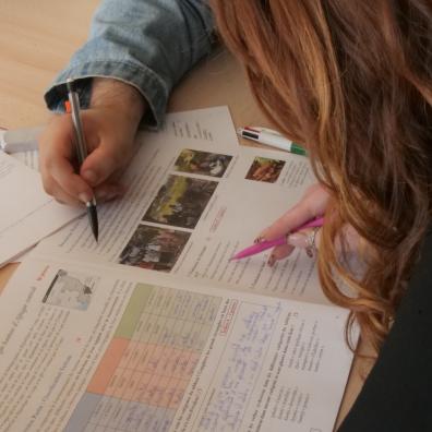 We see the hands of two people on a desk, working on written and illustrated documents.