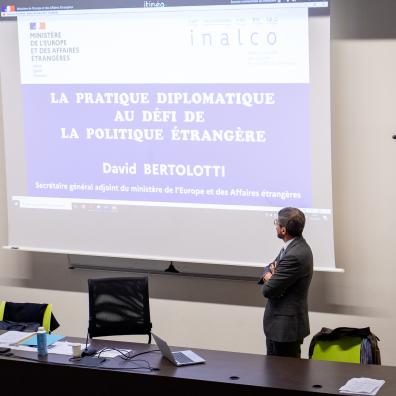 David Bertolotti, secrétaire général adjoint du ministère de l'Europe et des Affaires étrangères, se tient debout devant un écran de projection sur lequel est écrit le sujet de son intervention : "La pratique diplomatique au défi de la politique étrangère"