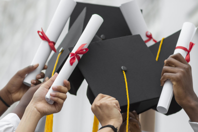 Mains d'étudiants qui tiennent des diplômes et des toques universitaires