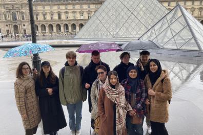 Un groupe de personnes posent devant les pyramides du Louvre, sous leurs parapluies