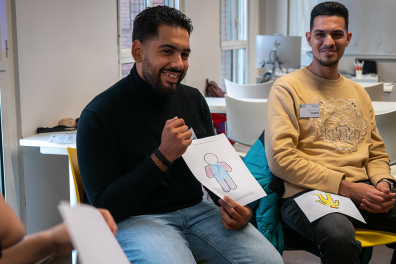 Deux hommes sont assis et participent à un atelier. L'un montre une feuille avec le dessin d'un bonhomme