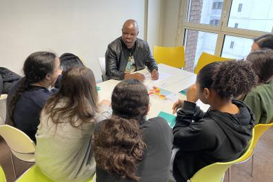 Un homme présente des documents à un groupe de personnes autour d'une table dans une salle de classe