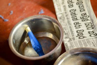 Dans un pot en métal se trouve une bobine de fil de couleur bleu, à côté d'une page de journal singhalais