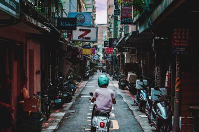 An alley in Tapei with a person on a motorcycle from behind