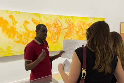 A man describes a card in front of a painting to two female visitors.