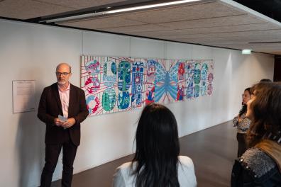 Un homme fait un discours devant une fresque et un public 