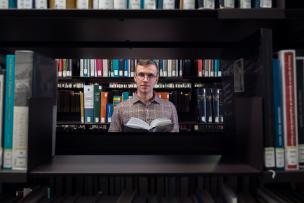 Jeune homme avec des lunettes en train de lire un livre dans une bibliothèque