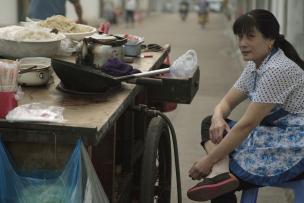 Une cuisinière de rue est assise sur un tabouret devant sa table dans les rues de Shanghai