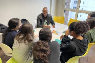 Un homme présente des documents à un groupe de personnes autour d'une table dans une salle de classe