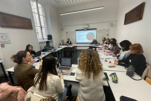 Un groupe de personne est installé dans une salle de classe en carrés avec une présentation powerpoint au tableau