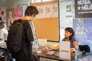 Un étudiant échange avec une dame assise à un Stan qui présente la Cinémathèque