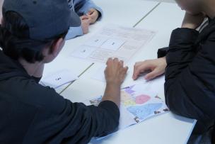 Des étudiants de dos sont assis entrain de travailler sur un bureau avec des documents
