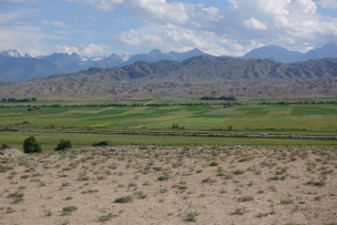 Paysage de sable, avec en arrière plan de l'herbe verte et une montagne