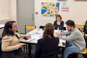 Groupe d'étudiants discutant autour d'une table, une carte est accrochée sur le mur derrière eux