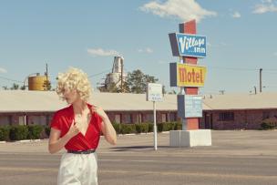 Photo of a blonde woman with curly hair in a motel parking lot