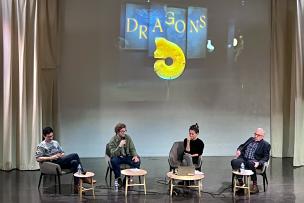 A stage on which 4 people are sitting with microphones in hand, talking to each other.